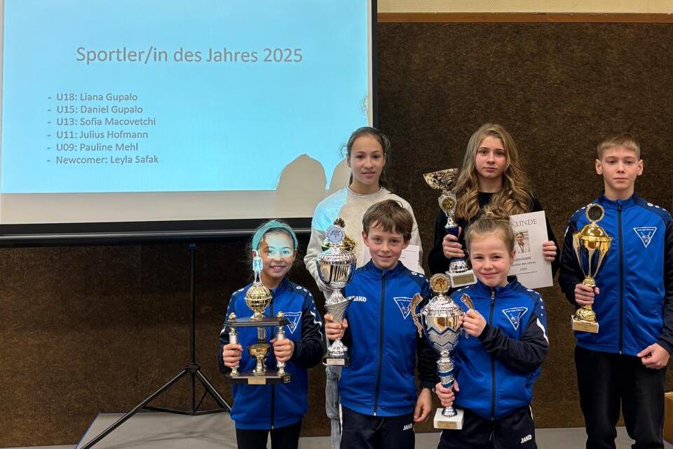 Sechs Kinder mit Pokalen vor einer Präsentationstafel, die die Sportler:innen des Jahres 2025 zeigt.